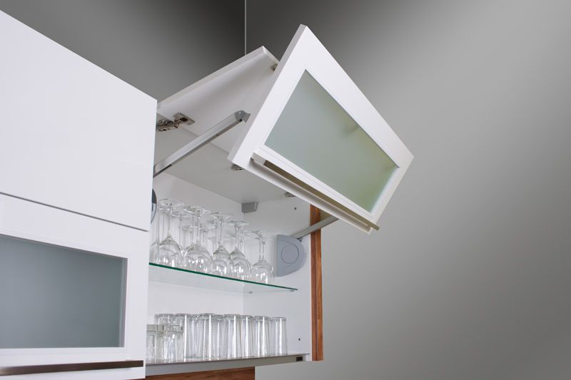 Weißer Hängeschrank mit hochgeklappter Tür, darin stehen Weingläser und Trinkgläser auf Glasböden.
